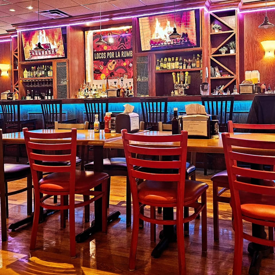 Interior of La Rumba Restaurant Latino with red chairs, wooden tables, and a bar with blue and purple neon lights.