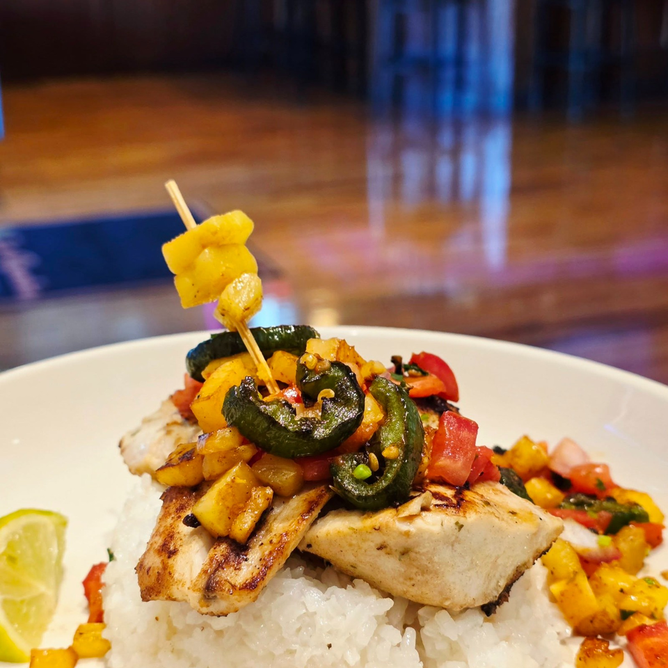 Grilled fish and vegetables served over white rice, topped with skewered yellow squash and garnished with lime.