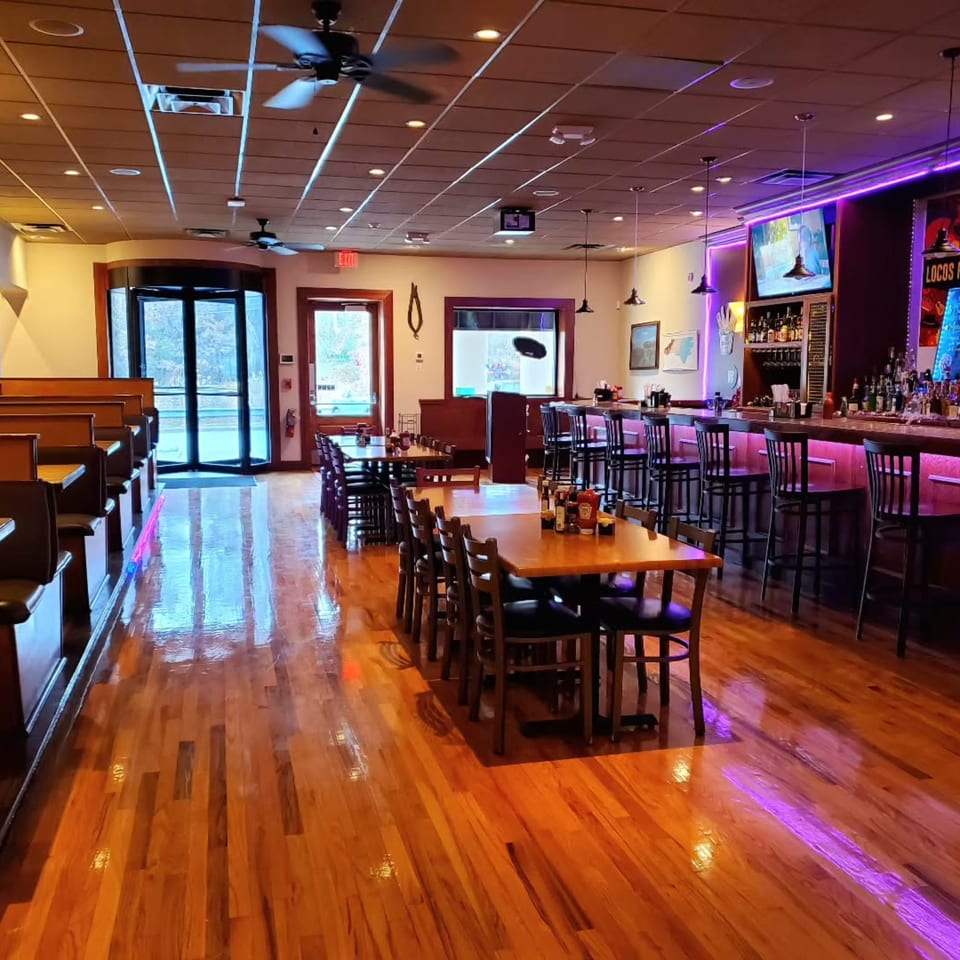 Interior of La Rumba Restaurant Latino, featuring a bar with purple lighting, dining tables, and booths.